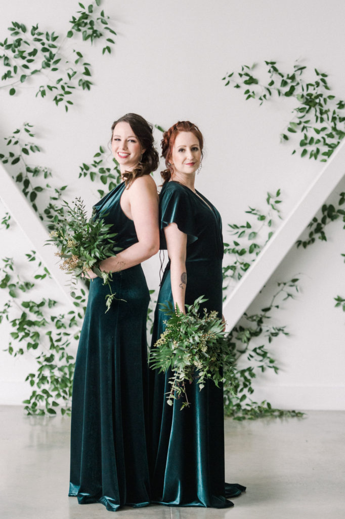 Bridesmaids in Jenny Yoo emerald green dresses standing back to back with green bouquets